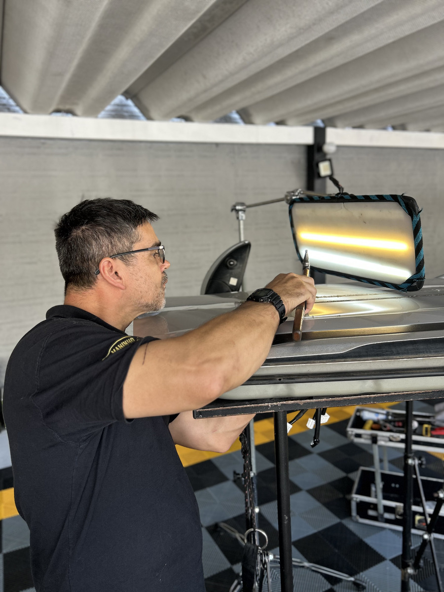 Técnico especializado em martelinho de ouro trabalhando em lataria de carro com luz de inspeção